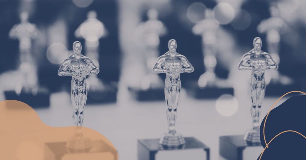 Escena elegante del Dolby Theatre en los Oscar 2025 con logo dorado 'Oscar 2025', trofeos y fondo negro con destellos rojos y dorados.